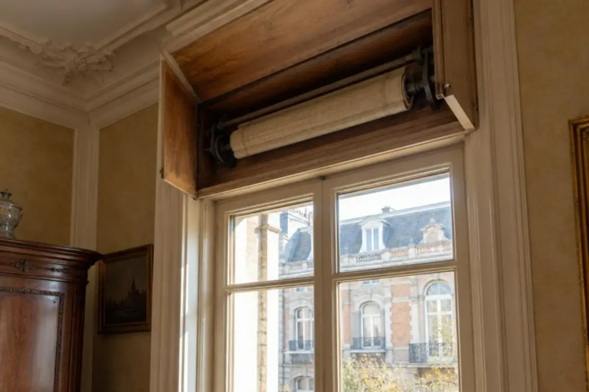 Coffre intérieur en bois ouvert au-dessus d'une haute fenêtre, axe et tablier enroulé apparents